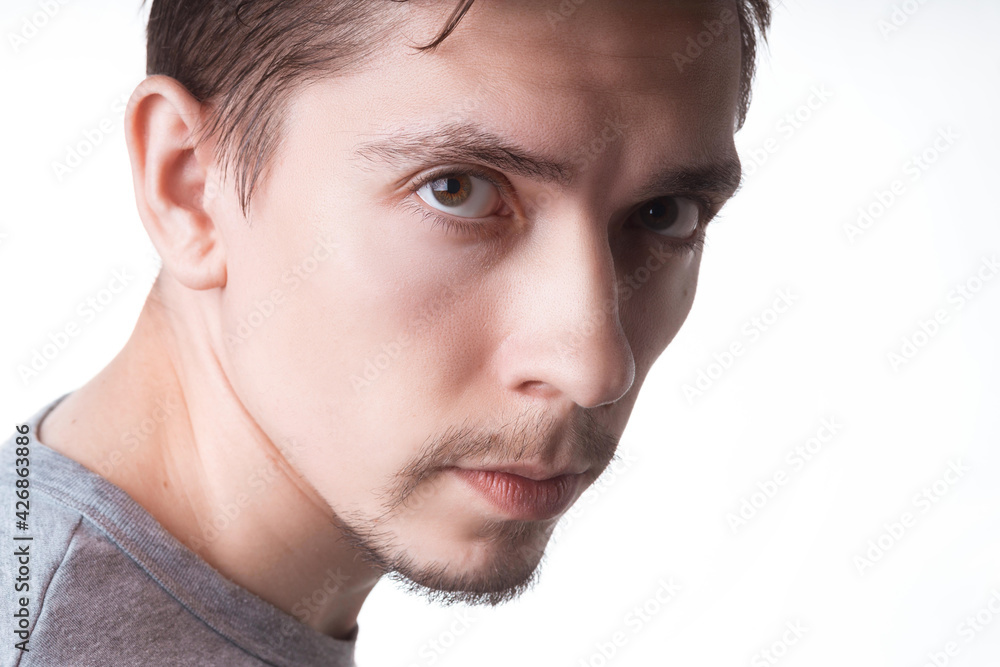 Obraz premium Portrait of a sensual young model in unlabeled gray t-shirt posing on white background. Serious man with small beard close-up portrait