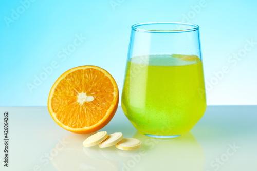 effervescent vitamin C pill dissolves in water. a glass of water, effervescent pill and orange on blue background. vitamin C concept