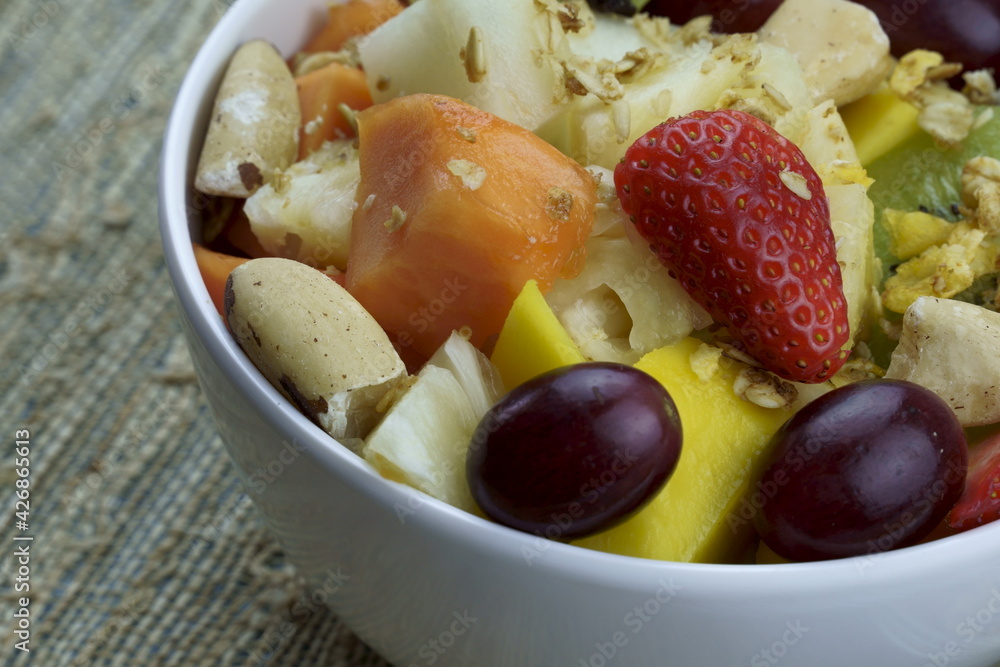 Fruit salad with chestnuts and granola in a bowl. Multicolored ripe fruits. Pineapple, mango, grape, strawberry, papaya, melon, banana and kiwi.. Fruit salad with chestnuts and granola in a bowl. Multicolored ripe fruits. Pineapple, mango, grape, strawberry, papaya, melon, banana and kiwi..