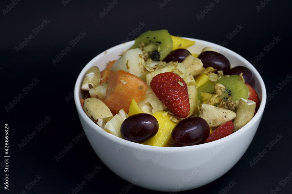 Fruit salad with chestnuts and granola in a bowl. Multicolored ripe fruits. Pineapple, mango, grape, strawberry, papaya, melon, banana and kiwi.. Fruit salad with chestnuts and granola in a bowl. Multicolored ripe fruits. Pineapple, mango, grape, strawberry, papaya, melon, banana and kiwi..