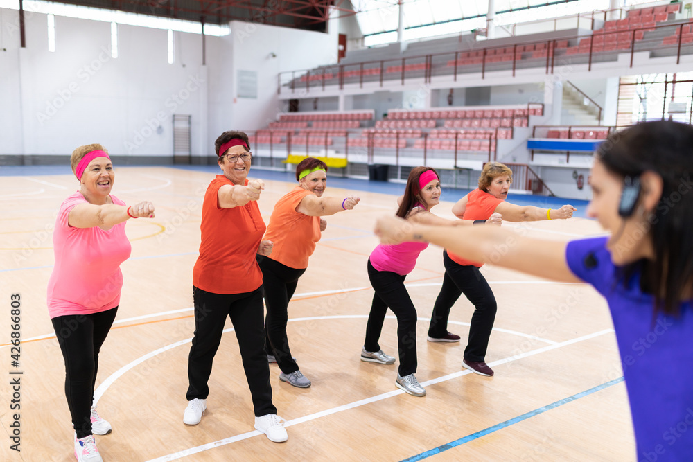 young girl sports monitor in sports center giving collective classes to older women for maintenance