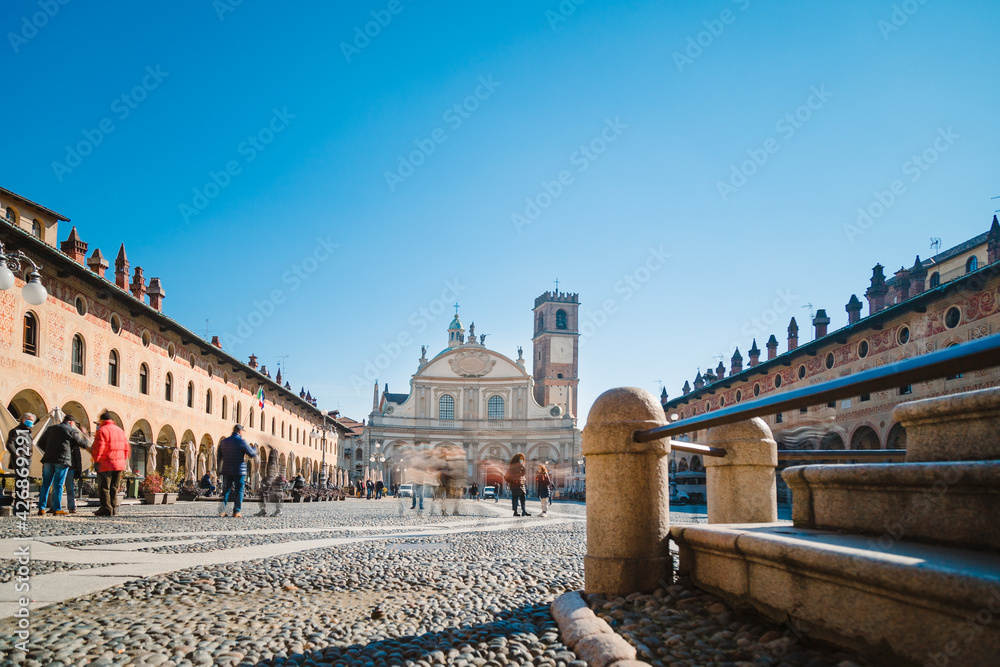 Vigevano, Italy - March 2021: square of the Cathedral of Sant'Ambrogio (Duomo di Vigevano) with people, long exposure, blue sky