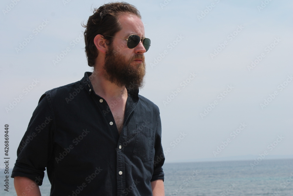 portrait of attractive man 30s with beard ocean sea behind him on sunny day 