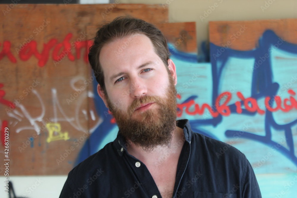 handsome man with beard in urban setting with graffiti background and dark navy shirt handsome man with beard in urban setting with graffiti background and dark navy shirt