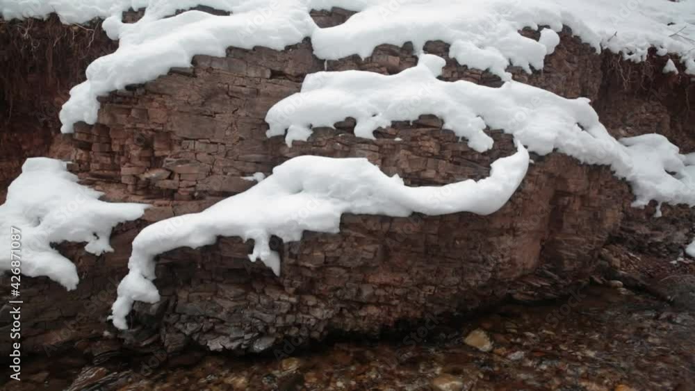 Layers of sedimentary rock form snow covered shelves above a small clear stream. Layers of sedimentary rock form snow covered shelves above a small clear stream.