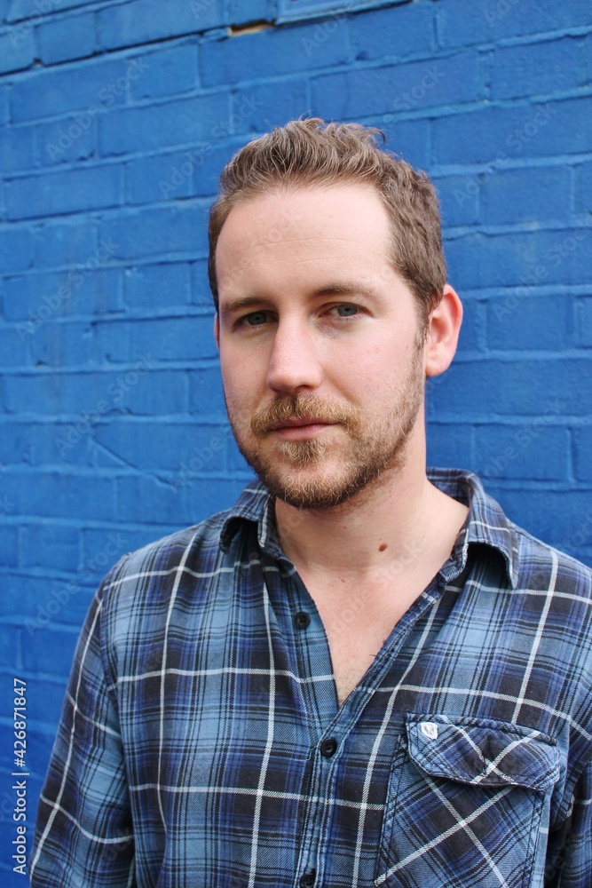 attractive male in blue plaid shirt against blue background painted wall relaxed and confident attractive male in blue plaid shirt against blue background painted wall relaxed and confident