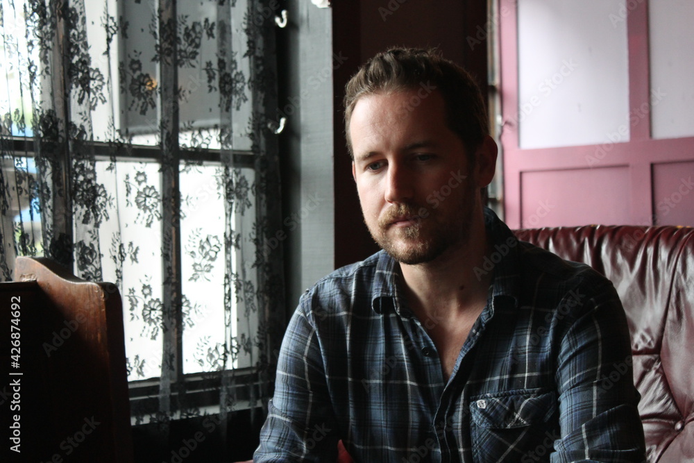 attractive male in blue plaid shirt relaxed and confident in living room sitting attractive male in blue plaid shirt relaxed and confident in living room sitting