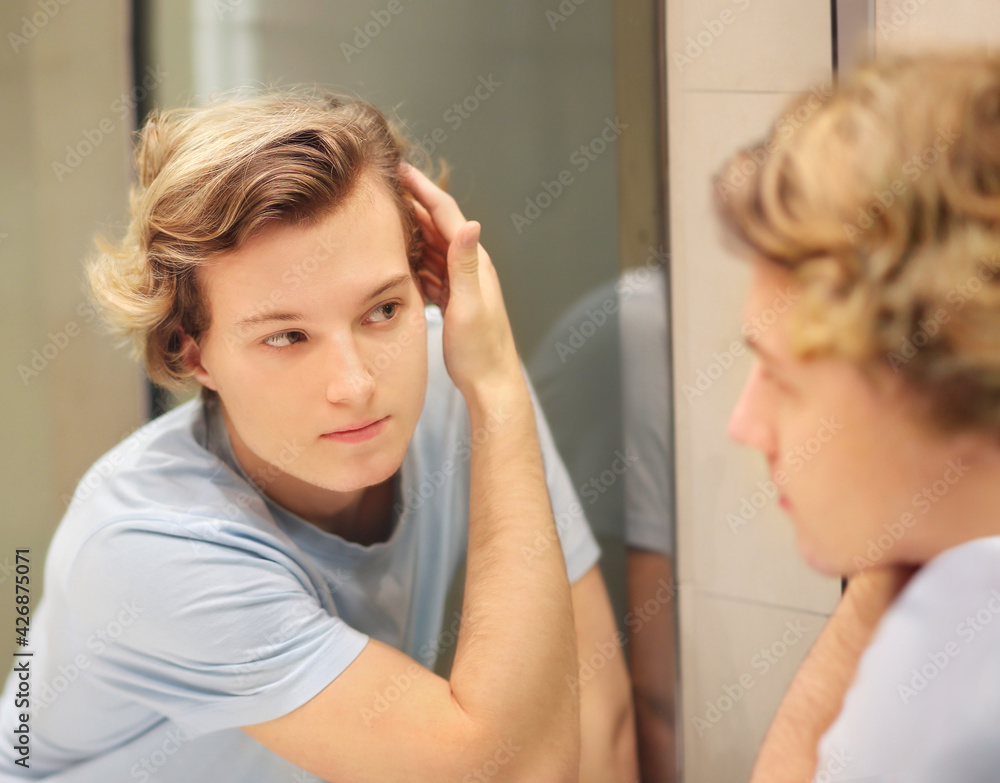young man looking in the mirror,combing his hair,looking at problems on face young man looking in the mirror,combing his hair,looking at problems on face