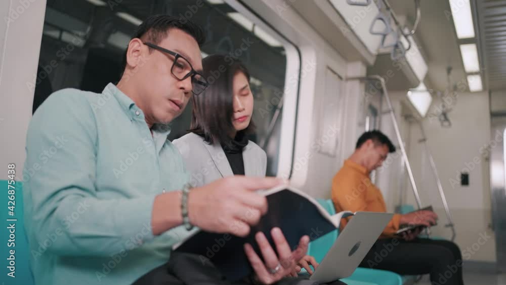 Businessman talking with businesswoman using laptop computer on the sky train or subway their way to working transportation people lifestyle concept. Businessman talking with businesswoman using laptop computer on the sky train or subway their way to working transportation people lifestyle concept.