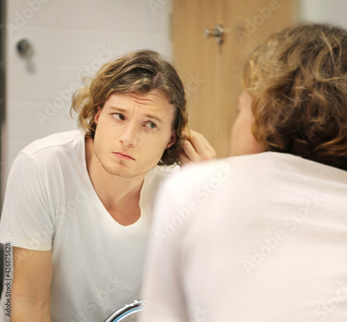 young man looking in the mirror,combing his hair,looking at problems on face..
