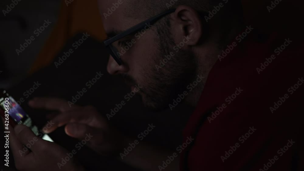 Bored Guy Lying In The Dark While Scrolling Feeds Through His Phone. Night insomnia. Portrait shot Bored Guy Lying In The Dark While Scrolling Feeds Through His Phone. Night insomnia. Portrait shot