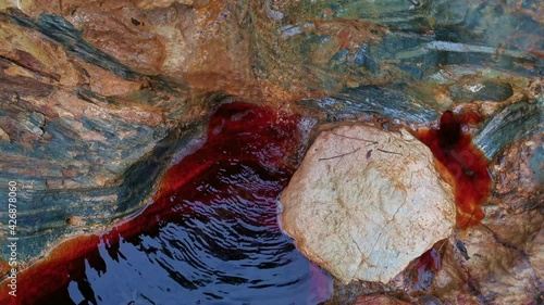 Reddish running water between rocks near the source of the Rio Tinto in Andalusia
