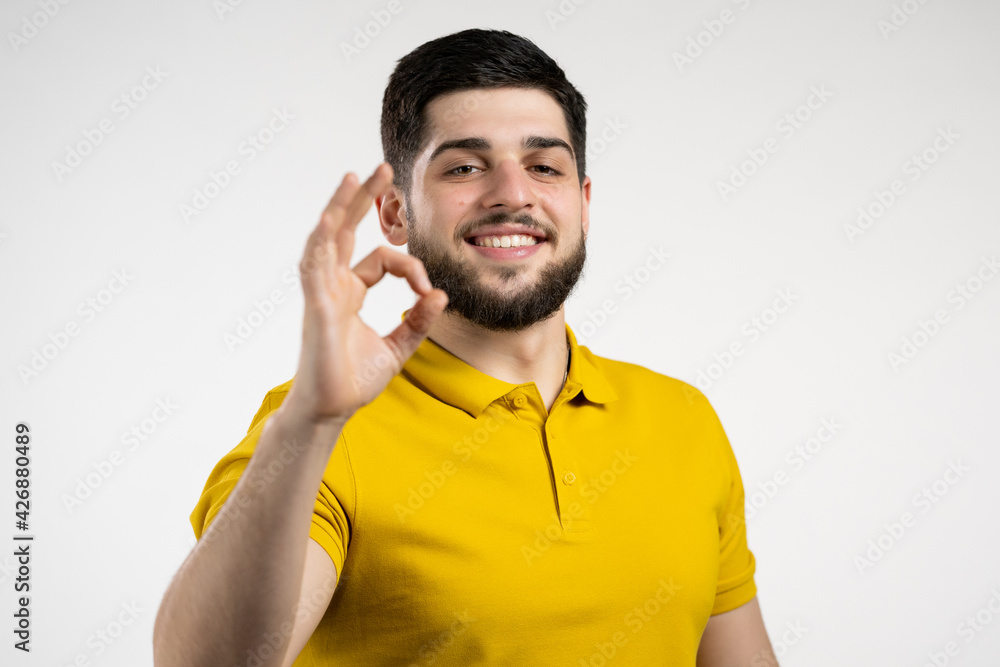 Handsome man in yellow wear shows okay, ok gesture. Happy guy on white background. Winner. Success. Positive male model smiles to camera. Body language. Handsome man in yellow wear shows okay, ok gesture. Happy guy on white background. Winner. Success. Positive male model smiles to camera. Body language.