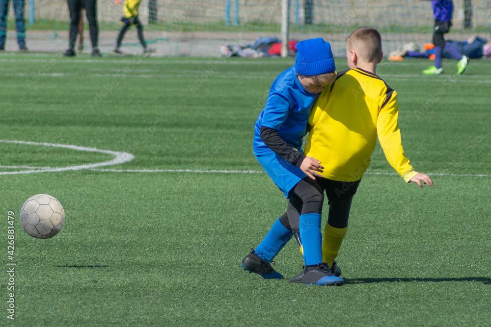 Fototapeta premium Children's football. Children are playing football. The active struggle and dynamics of the boys' soccer match. The boys are recklessly fighting for the ball