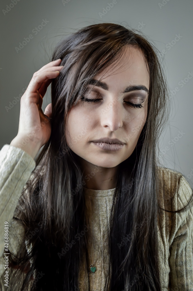 Portrait of a beautiful young woman with long brown hair who has a headache with her eyes closed Portrait of a beautiful young woman with long brown hair who has a headache with her eyes closed