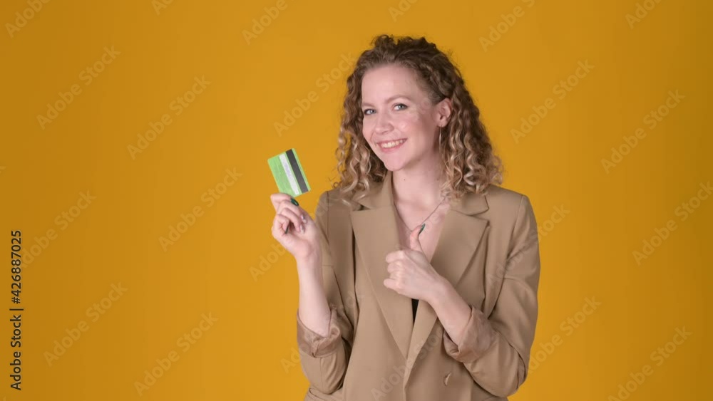 Cheerful young girl with curly hair Point hand on credit bank card showing thumb up like gesture isolated on yellow studio background. People lifestyle concept. Cheerful young girl with curly hair Point hand on credit bank card showing thumb up like gesture isolated on yellow studio background. People lifestyle concept.