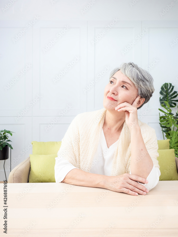 Senior asian woman with short grey hairstyle putting chin on hand and sitting at wood table. Senior asian woman with short grey hairstyle putting chin on hand and sitting at wood table.