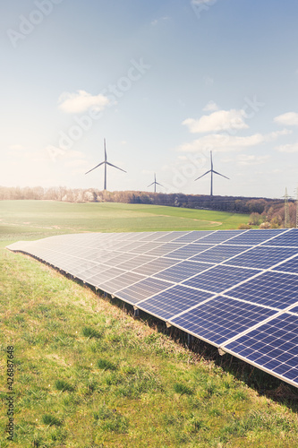 Photovoltaic park: Solar paneles with warm sunlight and wind turbines in the background. Renewable energies.