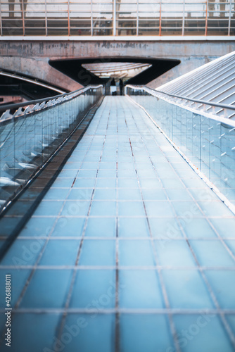 Vertical shot of a long modern overhead passage made of blue glass tiled blocks stretching into the distance with glass fence and chrome banister ending with a pedestrian tunnel of a railroad station © skyNext
