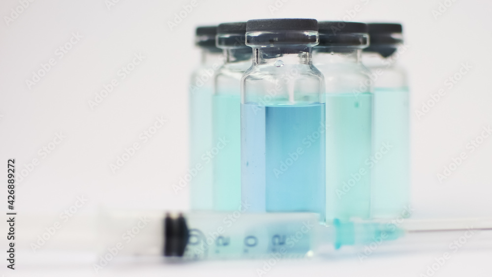 Vial vaccine, glass ampoules with transparent and blue liquid, a syringe is lying near on white background, global vaccination concept Vial vaccine, glass ampoules with transparent and blue liquid, a syringe is lying near on white background, global vaccination concept