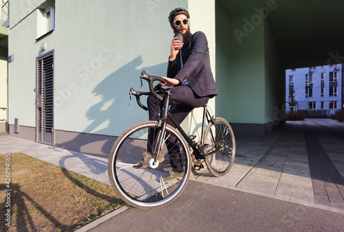 Start new day with fresh coffee. Millennial businessman holding cup of coffee and leaning at his bicycle, looking at free space.