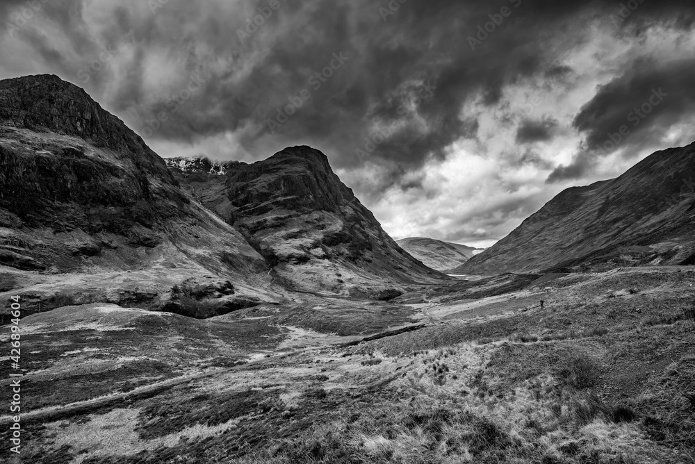 Majestic moody  black and white landscape image of Three Sisters in Glencoe in Scottish Highlands on a wet Winter day wit high water running down mountains
