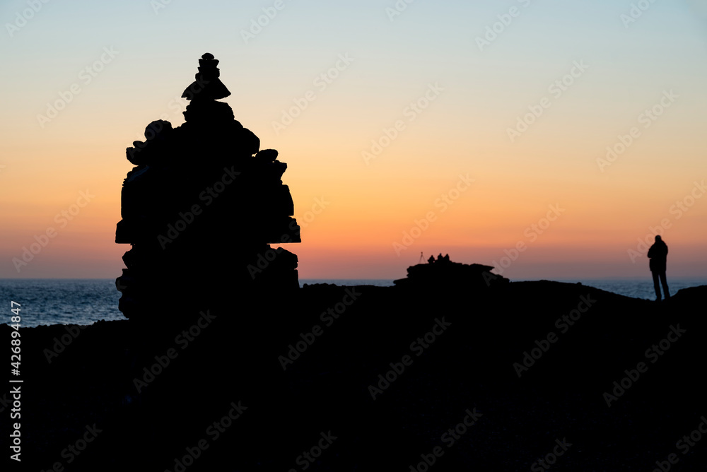 Beautiful silhouette landscape image of zen rock pile against vibrant peaceful sunset with photographers in background