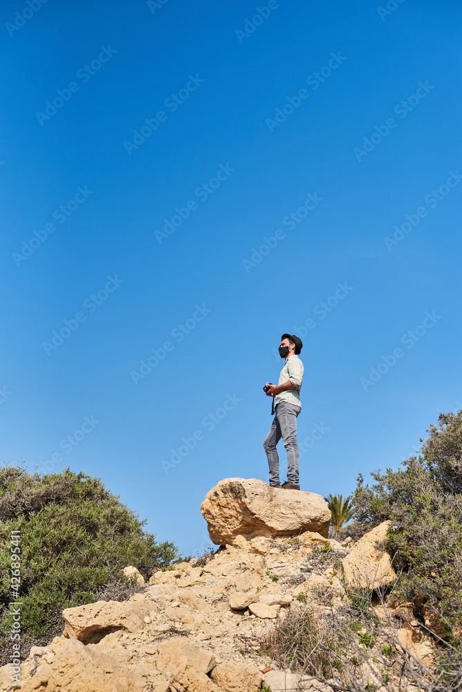 A tourist wears a face mask while taking a photo on top of a rock