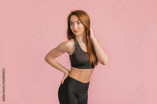 Fitness girl smiling in black sportswear on a pink background. Slim woman with a beautiful athletic body and tanned skin