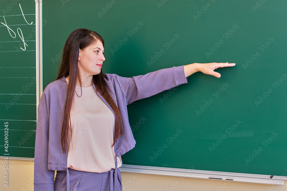 The young teacher points to the blackboard with her hand, copy space. The young teacher points to the blackboard with her hand, copy space.