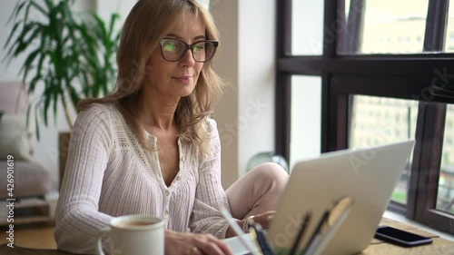 Woman using laptop for self education and sitting at table in apartment room.