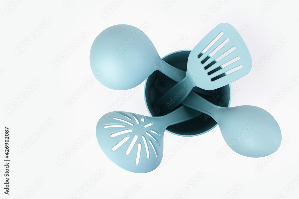 Fototapeta premium Blue plastic kitchen tools for cooking on a white background. Spatulas and ladles in a plastic container.