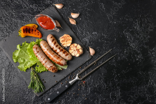 Slate plate with delicious grilled sausages on dark background