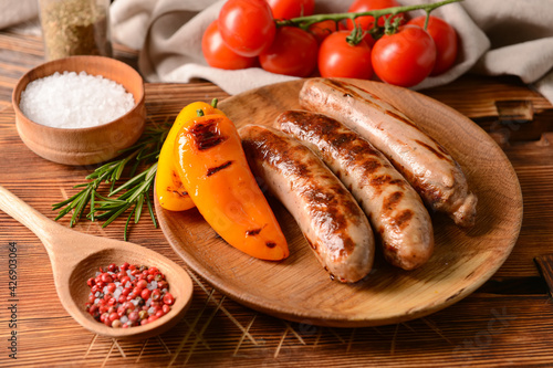Plate with delicious grilled sausages on wooden background
