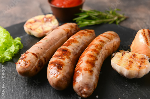 Slate plate with delicious grilled sausages on grunge background © Pixel-Shot