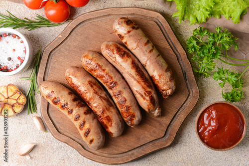 Board with delicious grilled sausages on wooden background