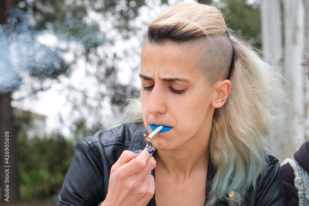 Young punk woman lighting up a cigarette in a park. Rock and roll lifestyle.