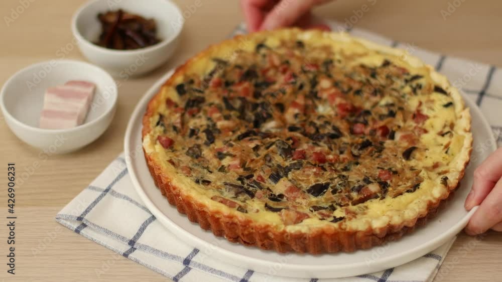 Homemade quiche lorraine with bacon, mushrooms and onions on the table. Female hands put dish with freshly baked pie Homemade quiche lorraine with bacon, mushrooms and onions on the table. Female hands put dish with freshly baked pie