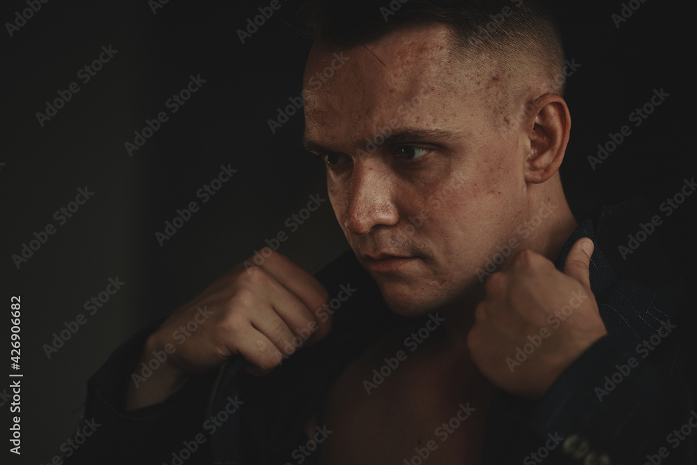 The man sits next to the wall looking forward, the room is dim. The man sits next to the wall looking forward, the room is dim.