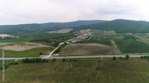 Upward flight of a drone over a vineyard and a highway in a valley
