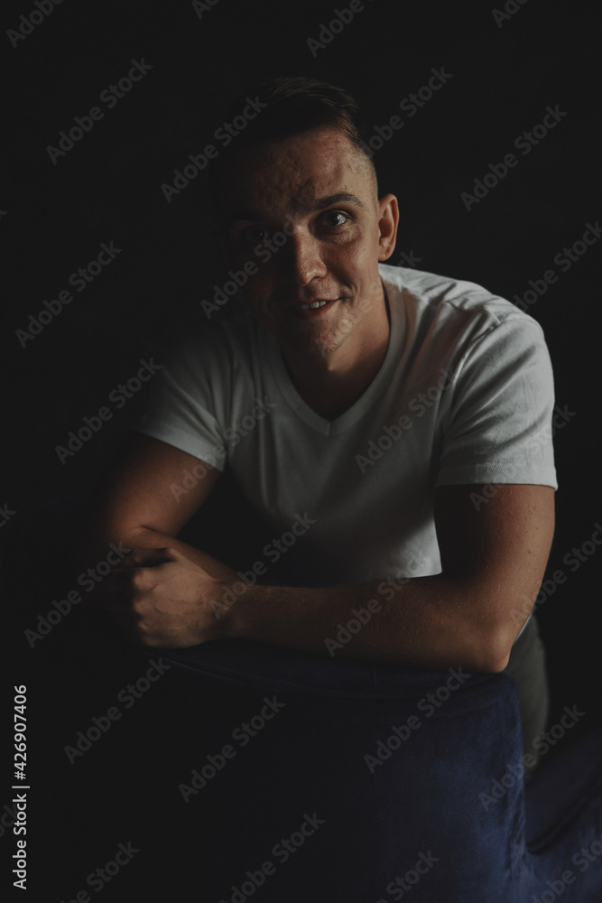 The man sits next to the wall looking forward, the room is dim. The man sits next to the wall looking forward, the room is dim.