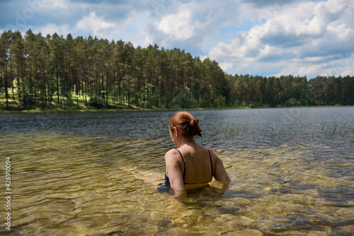 Fototapeta Naklejka Na Ścianę i Meble -  Dziewczyna wypoczywająca nad czystym jeziorem w promieniach letniego słońca, w tle zielony las.