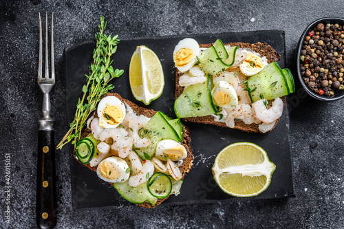 Fresh toasts with shrimp, prawns, quail eggs and cucumber on rye bread. Black background. top view