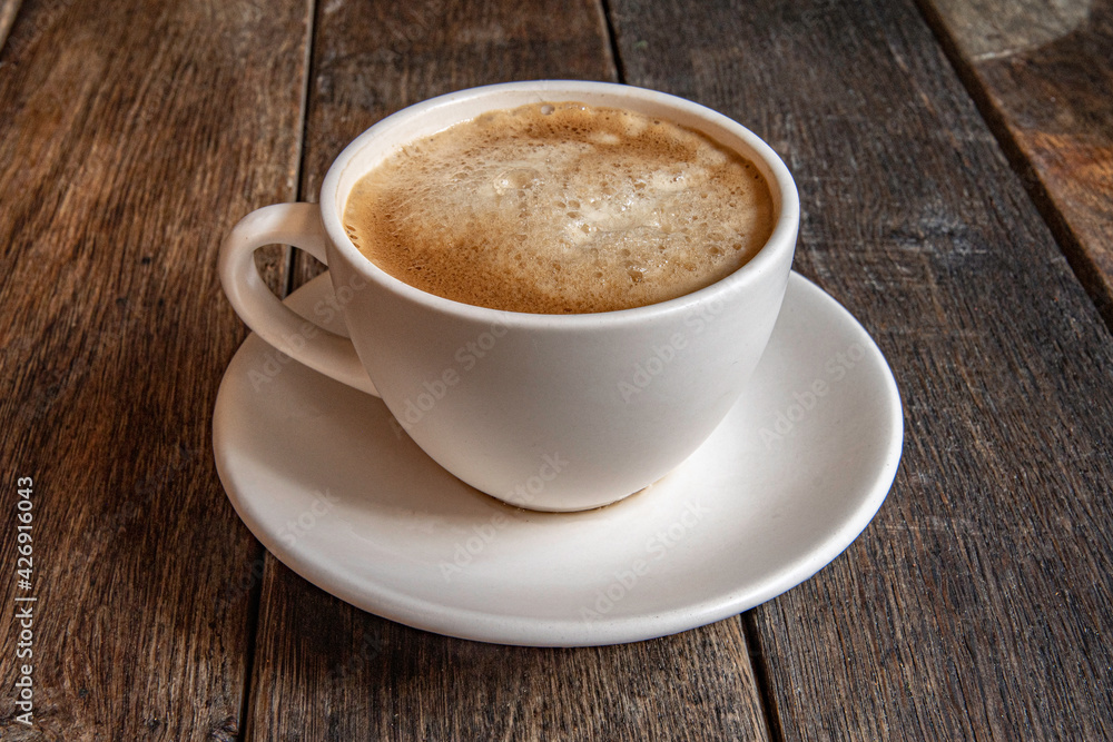 A cup of coffee on a saucer, on a wooden background.