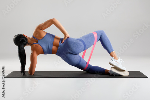 Fotografie, Tablou Fitness woman doing clamshell exercise for glutes with resistance band on gray background