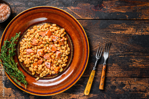 Kidney beans with smoked sausage and tomato sauce in a plate. Dark wooden background. Top view. Copy space