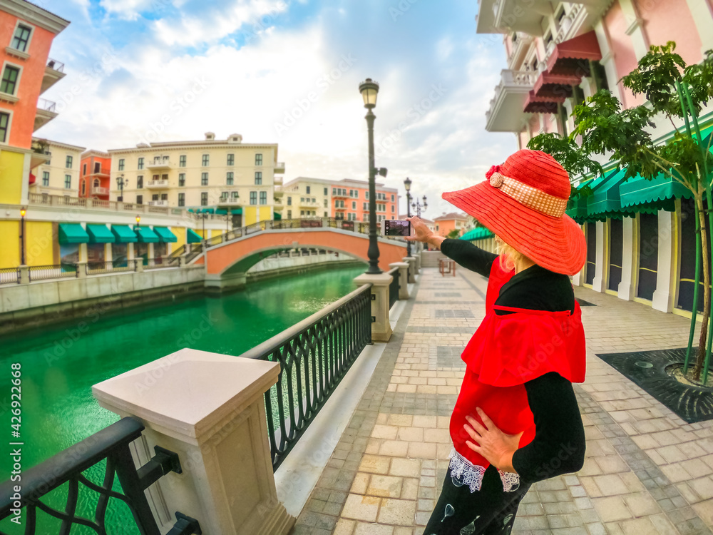 Φωτογραφία Woman in sunhat takes photo with smartphone of Venice, Venetian style waterfront village