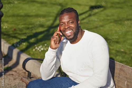 Happy black man talking on smart phone sitting in a park on a sunny day. 