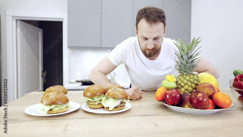 Young man is choosing between healthy food and fast food in the modern kitchen. Young man is choosing between healthy food and fast food in the modern kitchen.