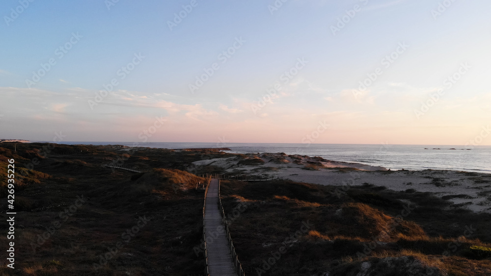 Aerial view of the Northern Litoral Natural Park in Ofir, Esposende, Portugal. Wooden boardwalk, sea, beach boulders and waves at sunset.